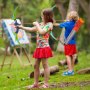 Kinder spielen draußen mit einem VEVOR-Bogenschießset für Kinder und zielen auf ein Ziel in einer üppig grünen Parklandschaft.