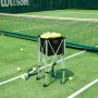 Tennisplatz mit einem mit Tennisbällen gefüllten VEVOR-Tennisballbehälter, neben einem Netz und einem Schläger.