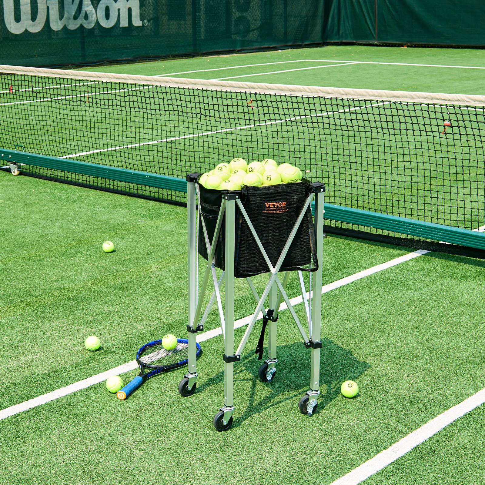 Tennisplatz mit einem mit Tennisbällen gefüllten VEVOR-Tennisballbehälter, neben einem Netz und einem Schläger.
