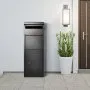 Caja de entrega de paquetes VEVOR instalada junto a una puerta de entrada moderna con planta en maceta y lámpara de pared.