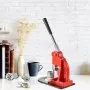 Máquina para hacer botones VEVOR sobre un escritorio blanco con libros antiguos, un jarrón, una taza y botones personalizados.