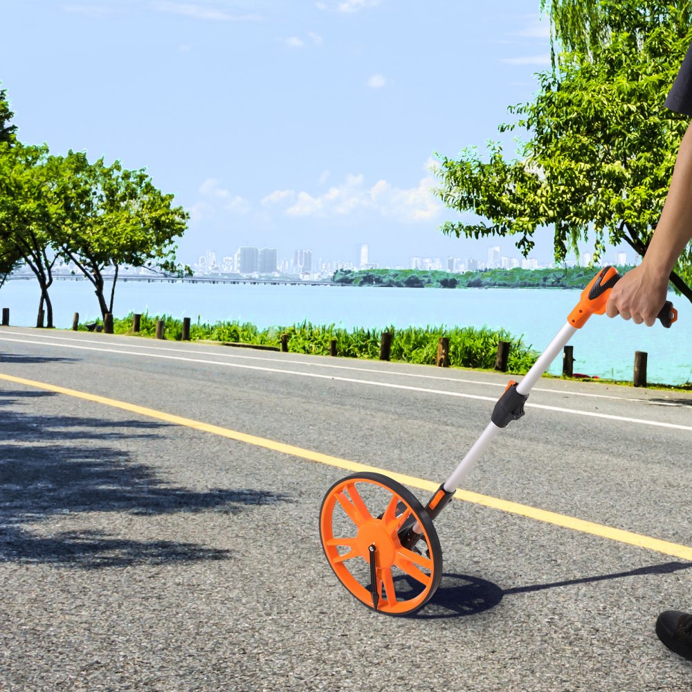 Persona que utiliza la rueda de medición VEVOR en una carretera costera con un horizonte de ciudad y frondosos árboles en el fondo.
