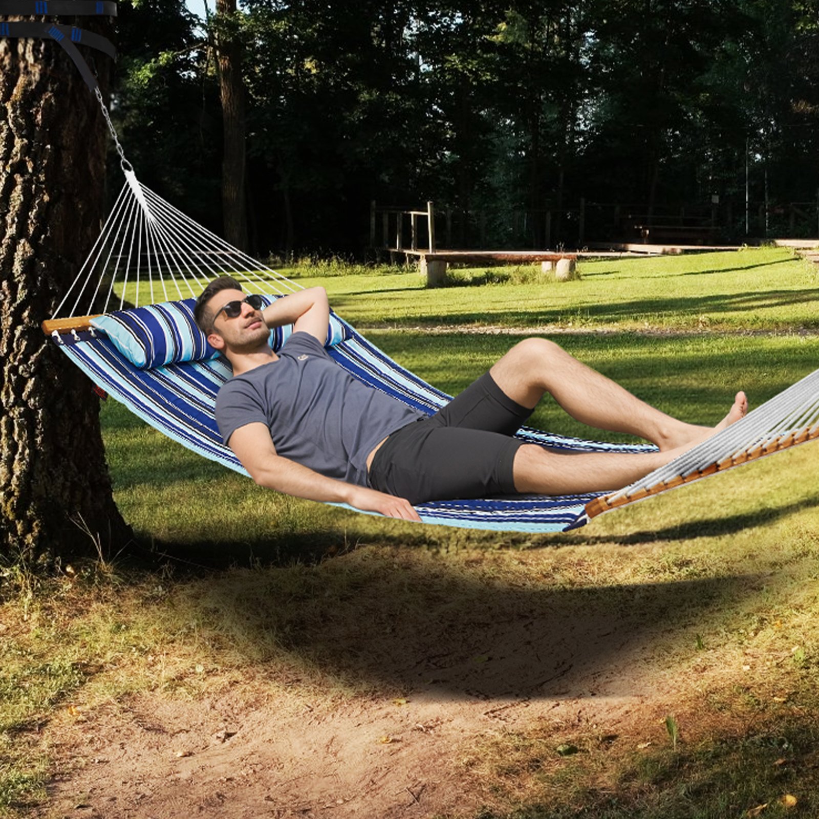Hombre descansando en una hamaca doble VEVOR en un parque al aire libre con césped, disfrutando del tiempo de relajación.