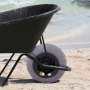 Carretilla negra en la playa de arena con ruedas de globo de playa VEVOR y el océano de fondo.