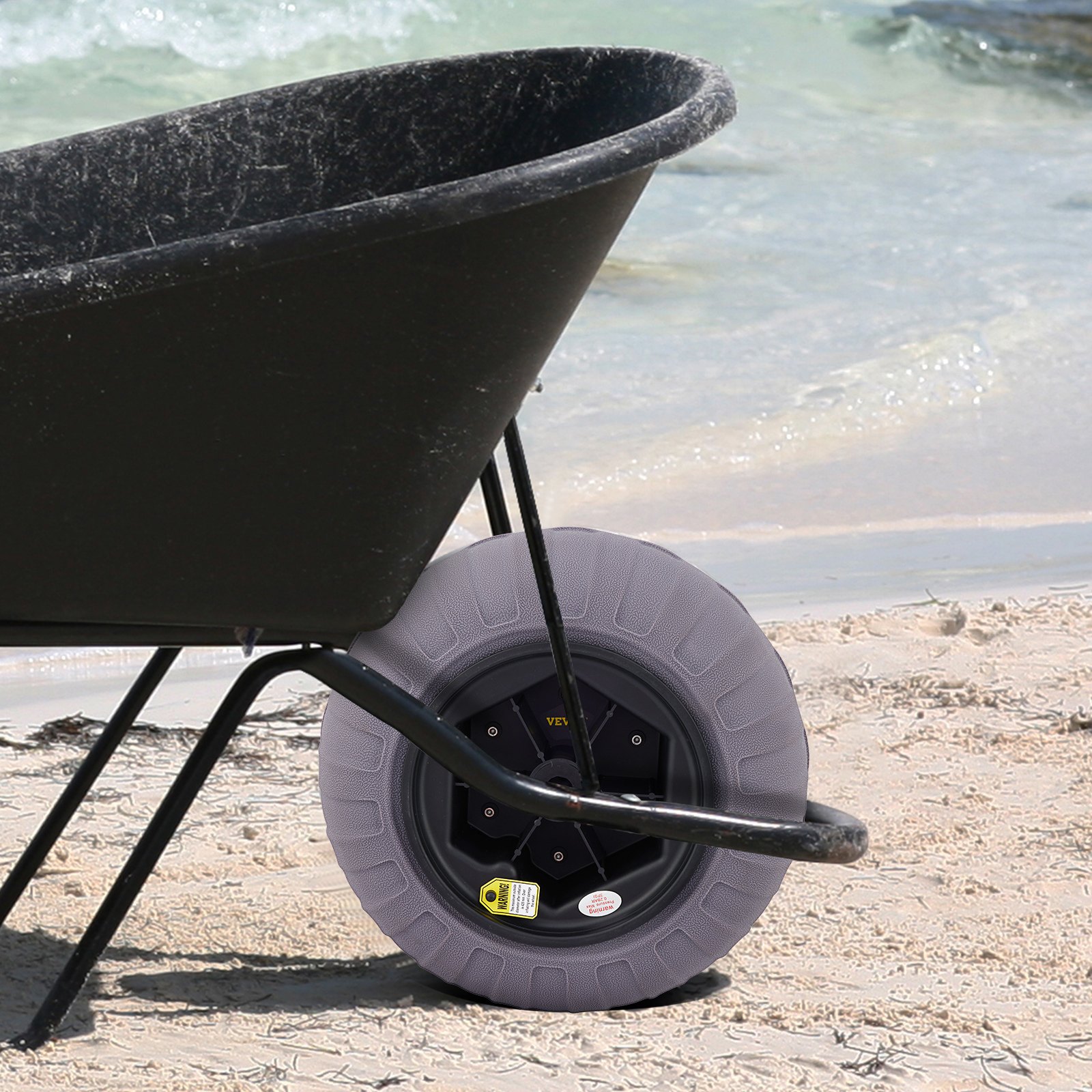 Carretilla negra en la playa de arena con ruedas de globo de playa VEVOR y el océano de fondo.