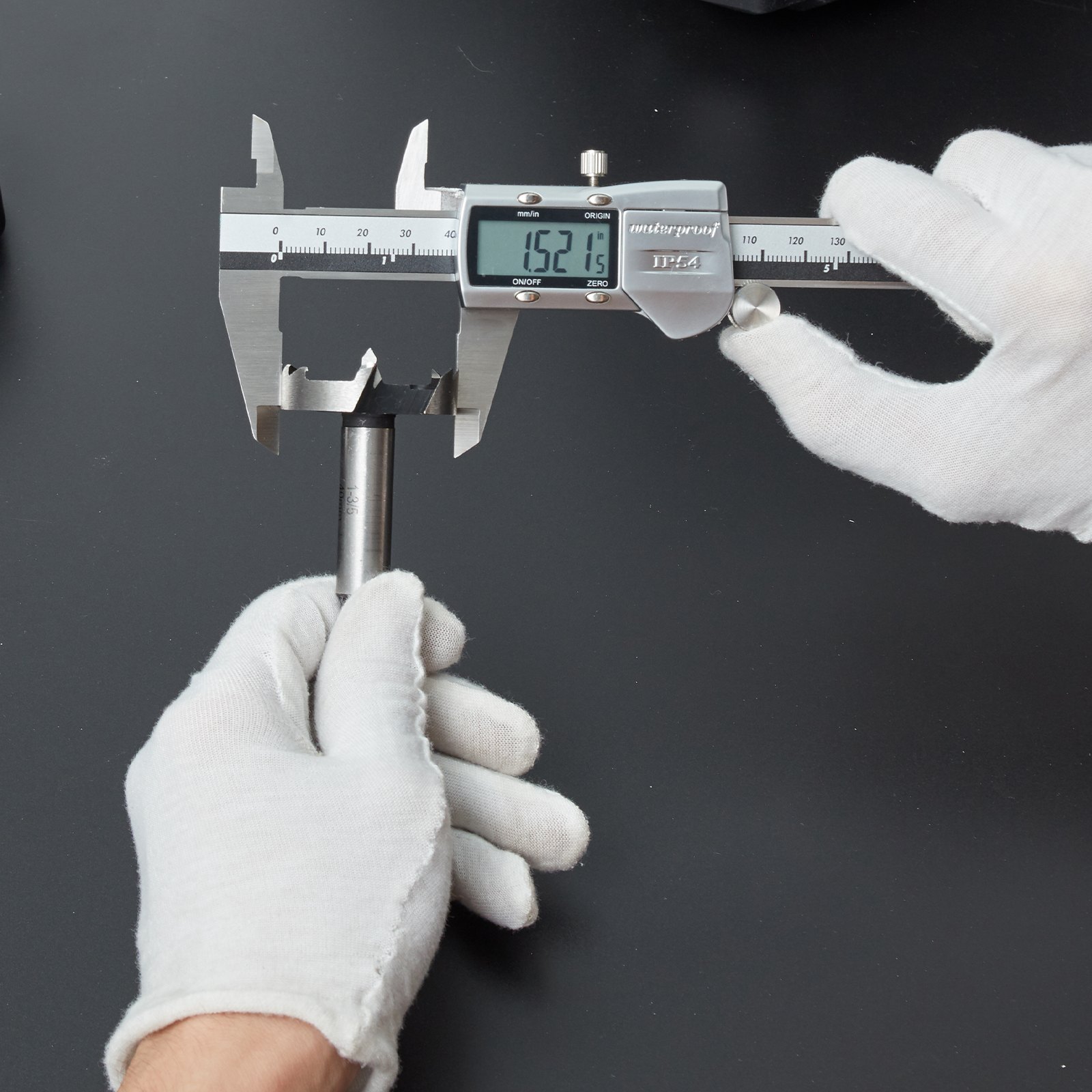 mano enguantada que utiliza un calibrador digital VEVOR para medir una varilla de metal en una superficie oscura.