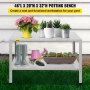 Banco para macetas VEVOR con plantas, botas, regadera y herramientas de jardinería sobre césped verde.