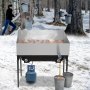 Bandeja evaporadora de jarabe de arce VEVOR en un bosque nevado con baldes recolectores de savia y tanque de propano azul
