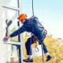 Limpiador de ventanas que utiliza cuerda de protección contra caídas VEVOR y casco naranja para mayor seguridad.