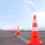 Conos de tráfico VEVOR alineados en una carretera vacía contra un cielo azul claro.