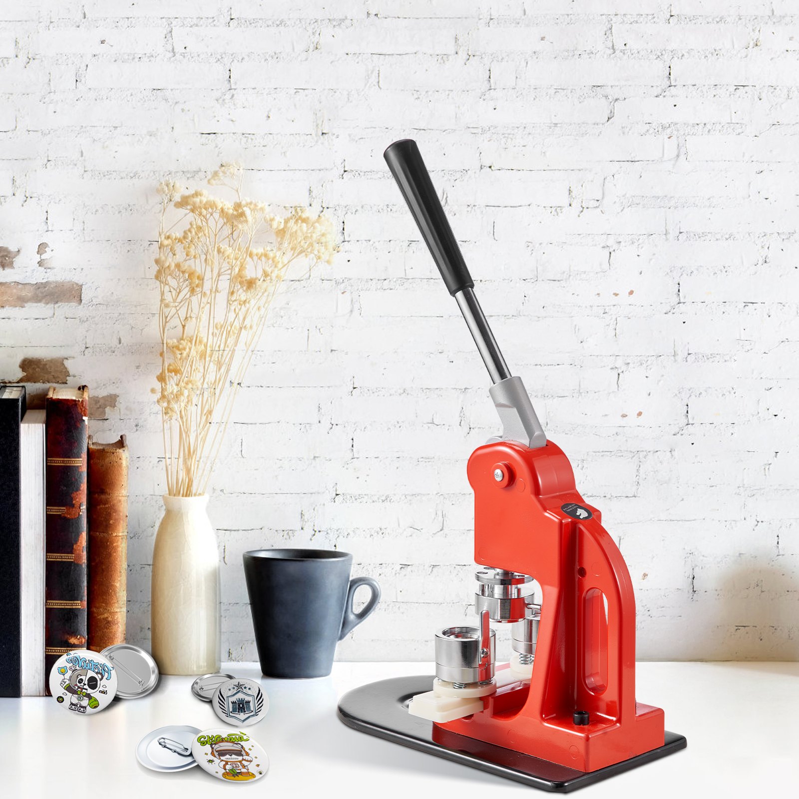 Máquina para hacer botones rojos VEVOR sobre una mesa blanca con libros, una taza y botones terminados cerca.