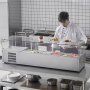 Un chef utiliza la estación de preparación de condimentos refrigerada VEVOR con varios ingredientes frescos en una cocina comercial.
