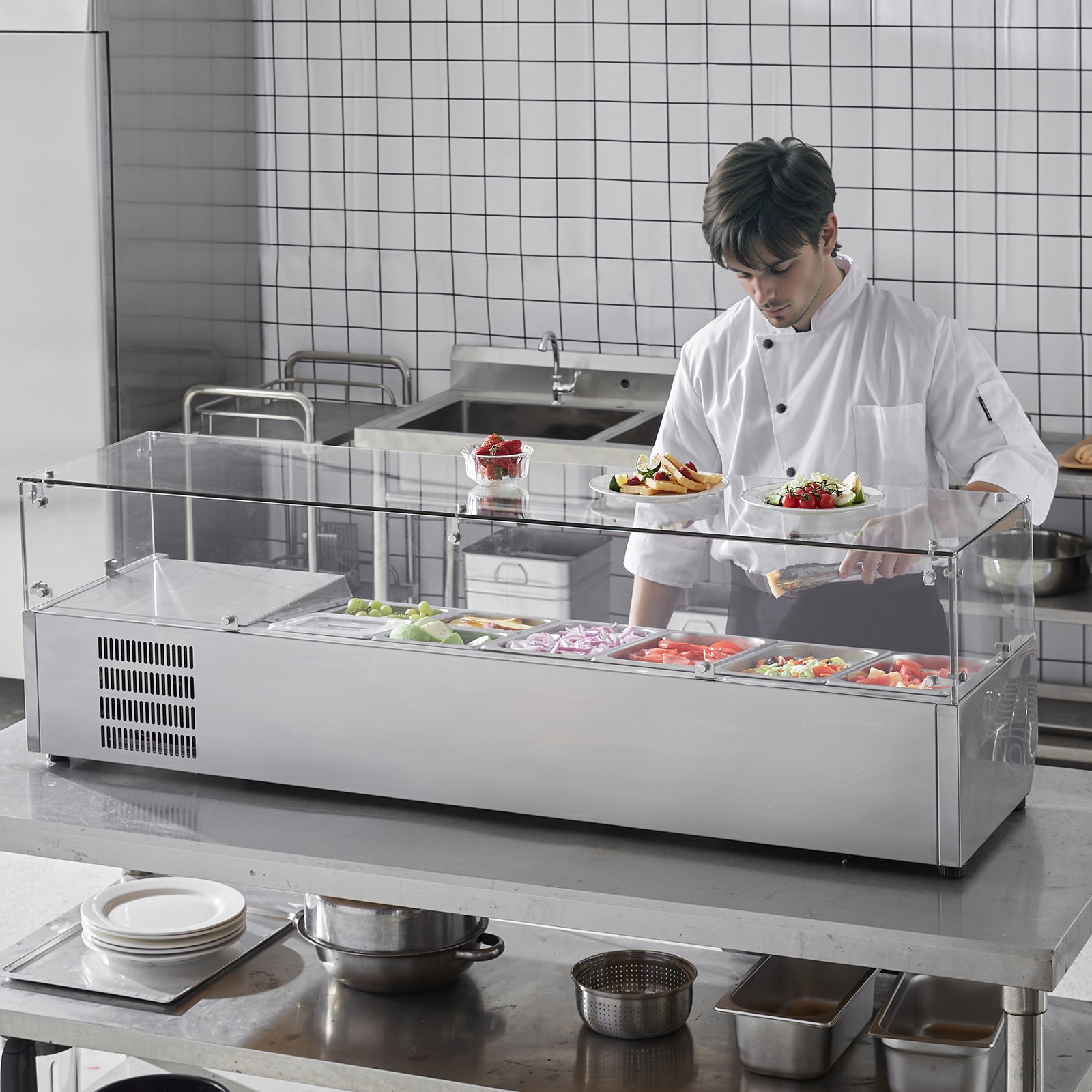 Un chef utiliza la estación de preparación de condimentos refrigerada VEVOR con varios ingredientes frescos en una cocina comercial.