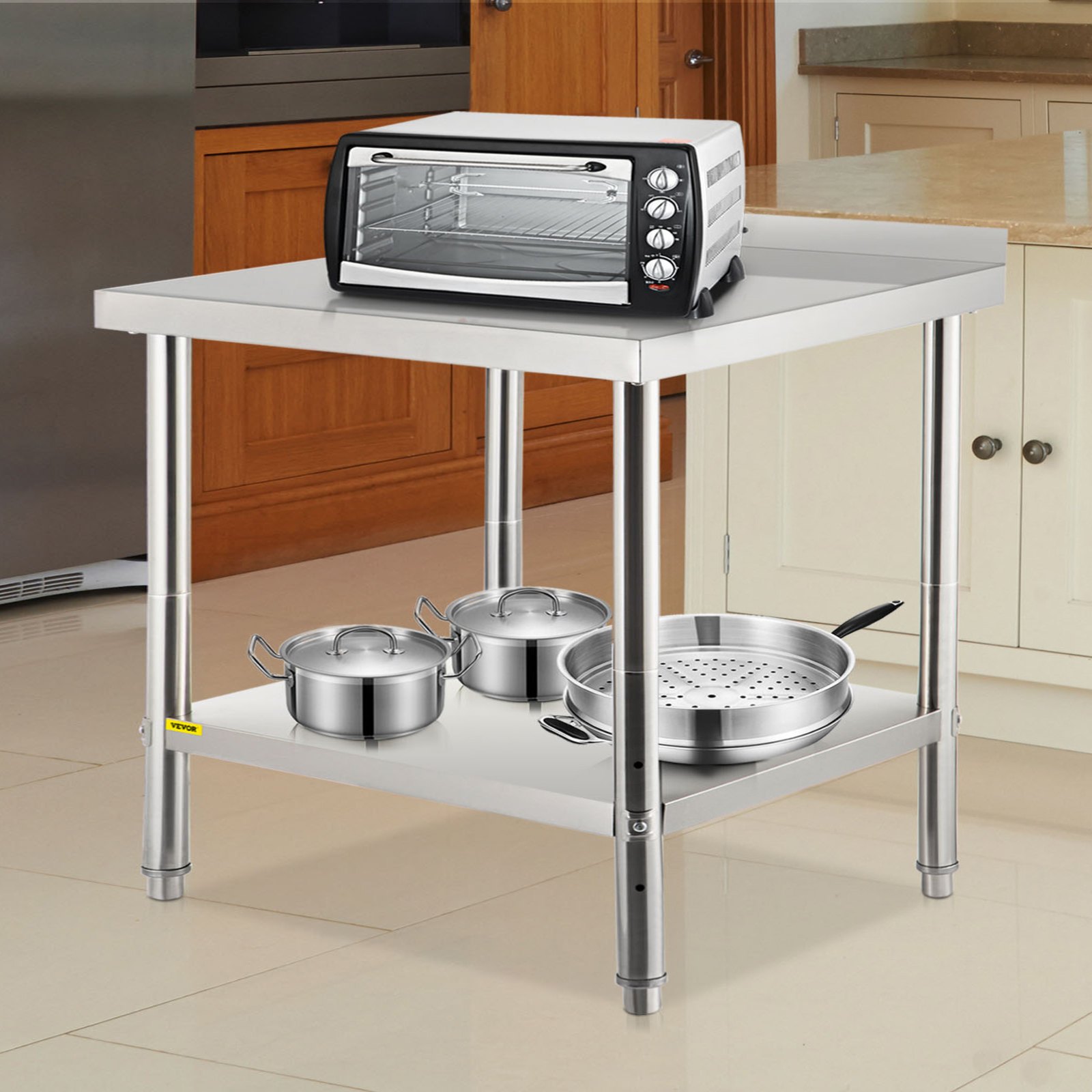 Mesa de preparación de acero inoxidable VEVOR con ollas, sartenes y un pequeño horno en una cocina moderna.