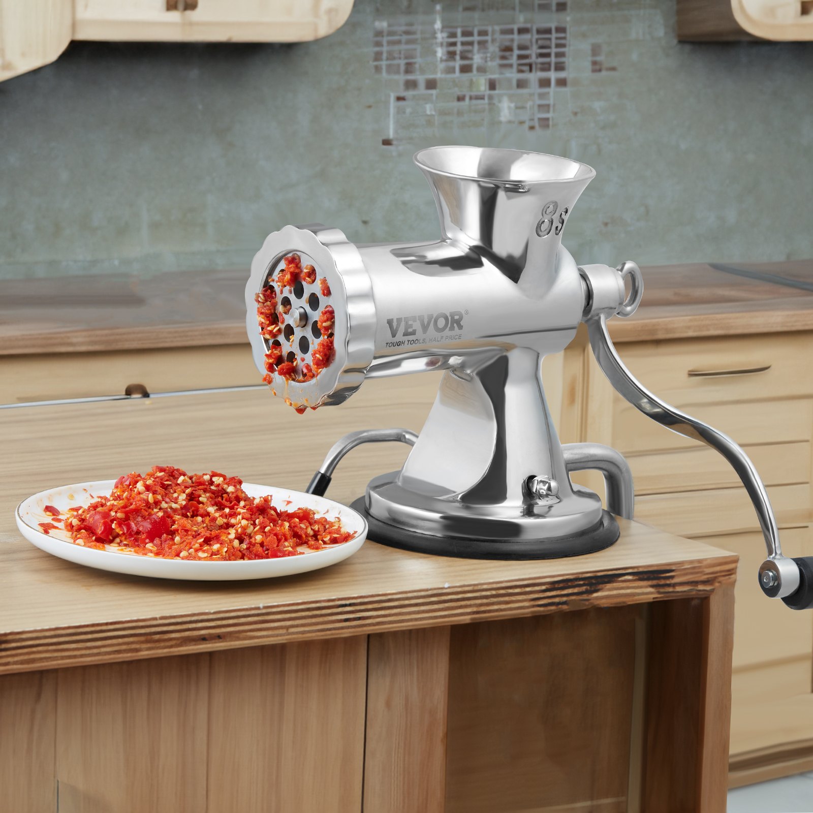 Picadora de carne manual VEVOR procesando pimientos rojos en una encimera de cocina de madera.