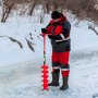 Persona que utiliza la barrena perforadora de hielo VEVOR en un lago congelado en invierno.