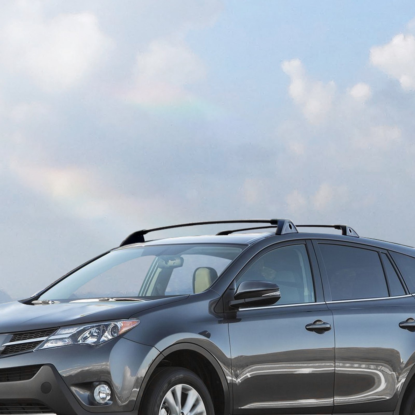SUV gris con barras transversales de techo VEVOR bajo un cielo azul con nubes.