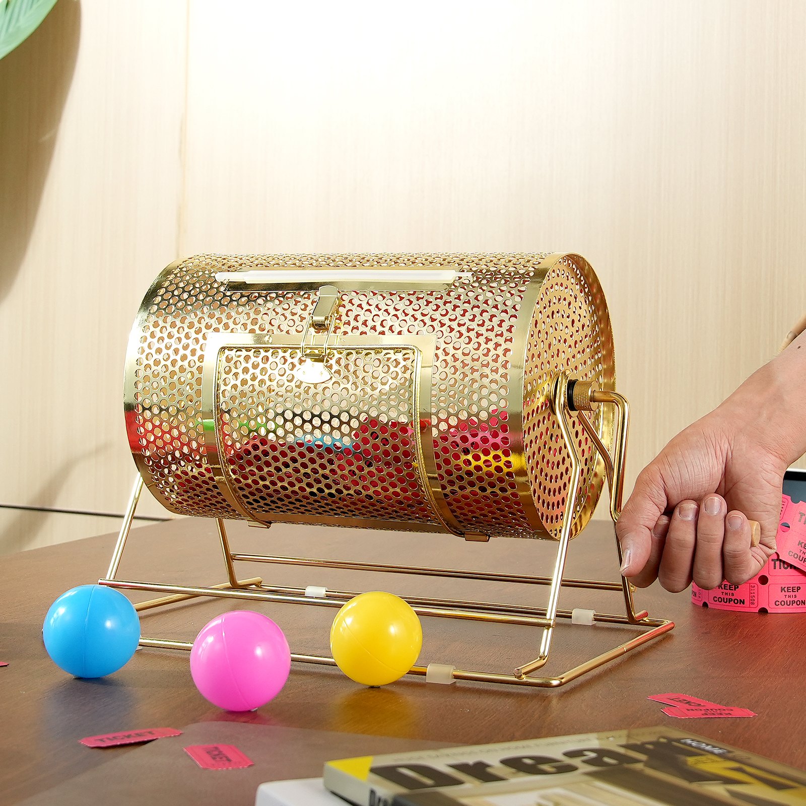 Tambor de rifa VEVOR dorado con bolas de colores sobre una mesa de madera y mango girando a mano.