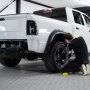 Mecánico trabajando en una camioneta blanca elevada en un garaje con suelo de baldosas de garaje VEVOR.