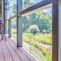 terraza con un kit de barandilla de cable VEVOR con vista a un pintoresco paisaje verde, con taburetes y piso de madera.