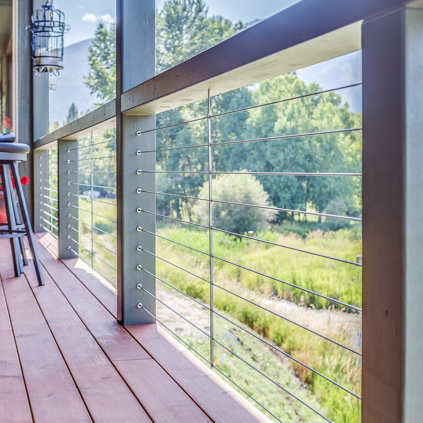 terraza con un kit de barandilla de cable VEVOR con vista a un pintoresco paisaje verde, con taburetes y piso de madera.