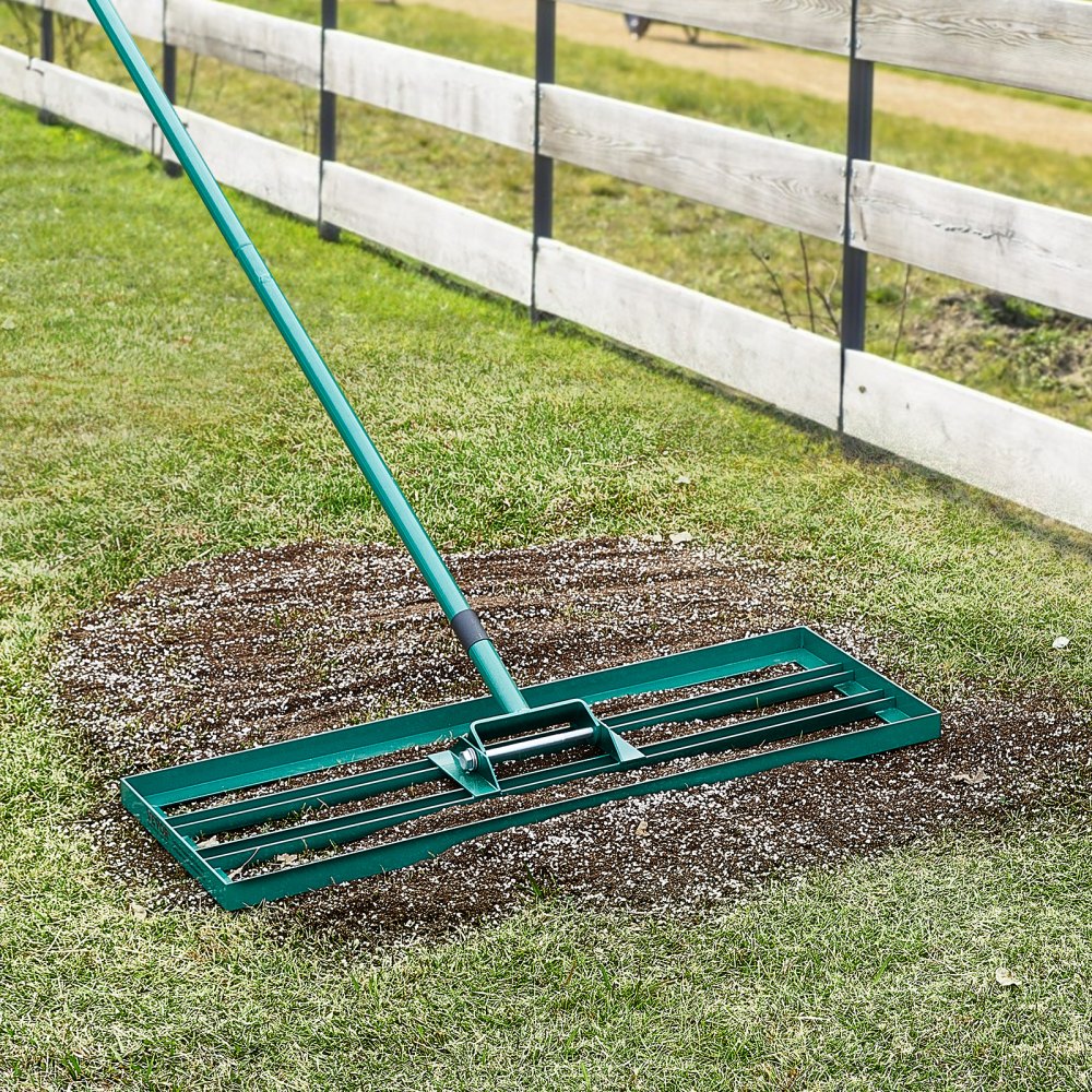 Rastrillo nivelador de césped VEVOR que extiende tierra sobre un césped cerca de una cerca de madera.