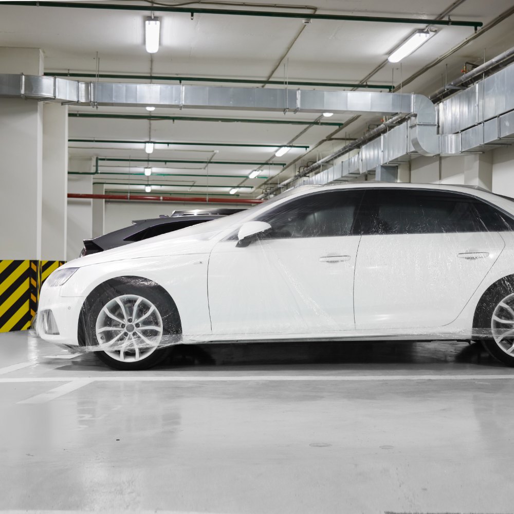 Coche blanco en un aparcamiento subterráneo cubierto con una funda para coche VEVOR.