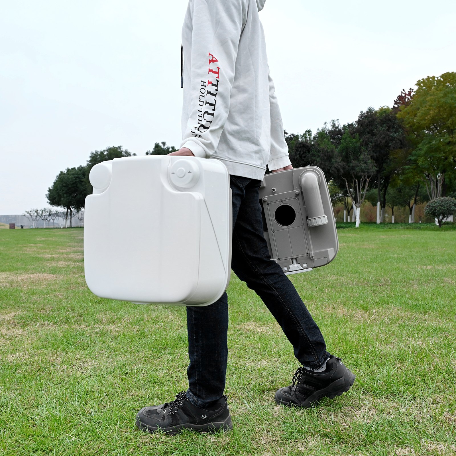 Persona que transporta un baño portátil VEVOR en un parque, mostrando la facilidad de transporte.