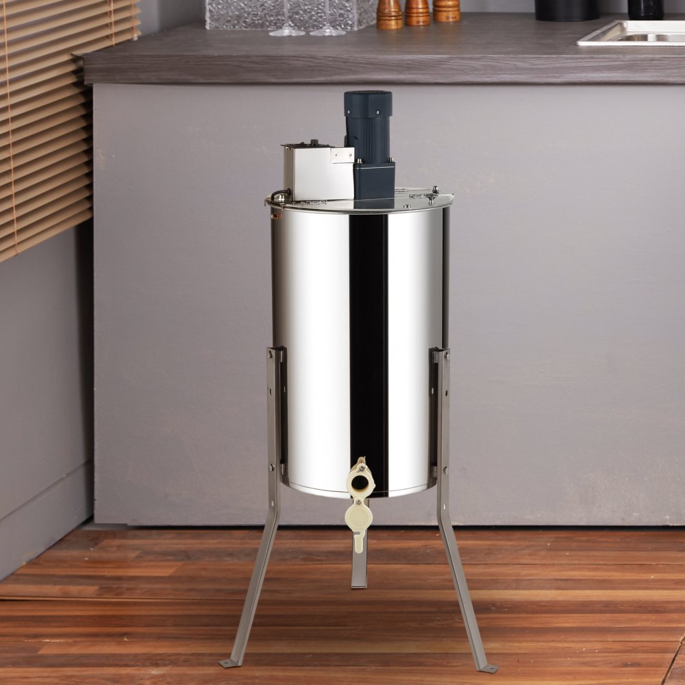 Extractor de miel VEVOR de acero inoxidable sobre suelo de madera en un entorno de cocina moderno.