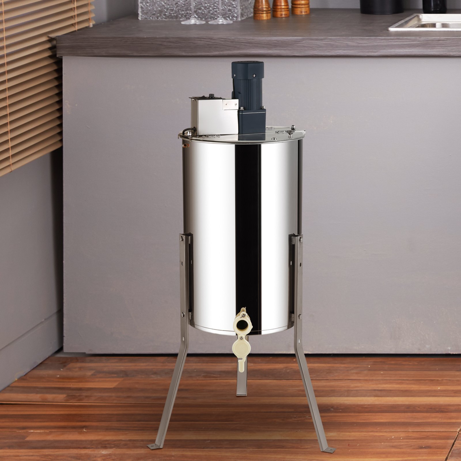 Extractor de miel VEVOR de acero inoxidable sobre suelo de madera en un entorno de cocina moderno.