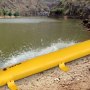 Barrera contra inundaciones VEVOR amarilla que protege una orilla de las olas de agua con un paisaje montañoso al fondo.