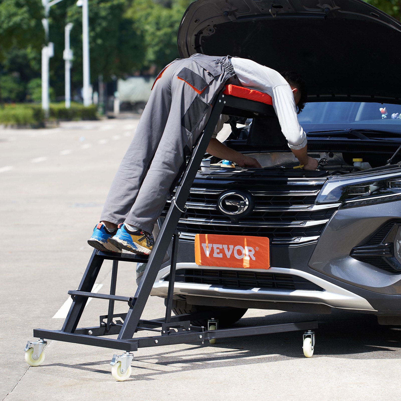Mecánico que utiliza la plataforma elevadora automotriz VEVOR para trabajar en el motor del automóvil en un entorno al aire libre.