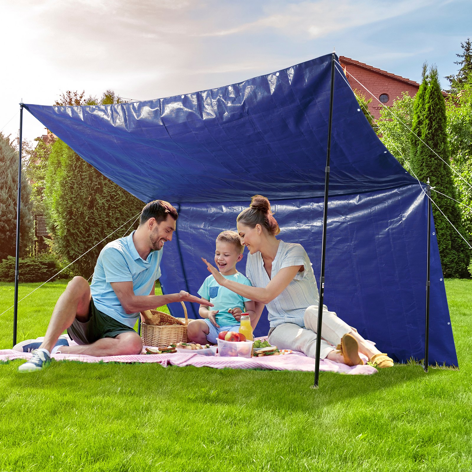 Familia disfrutando de un picnic bajo una lona impermeable VEVOR en un patio trasero, con comida sobre una manta rosa.