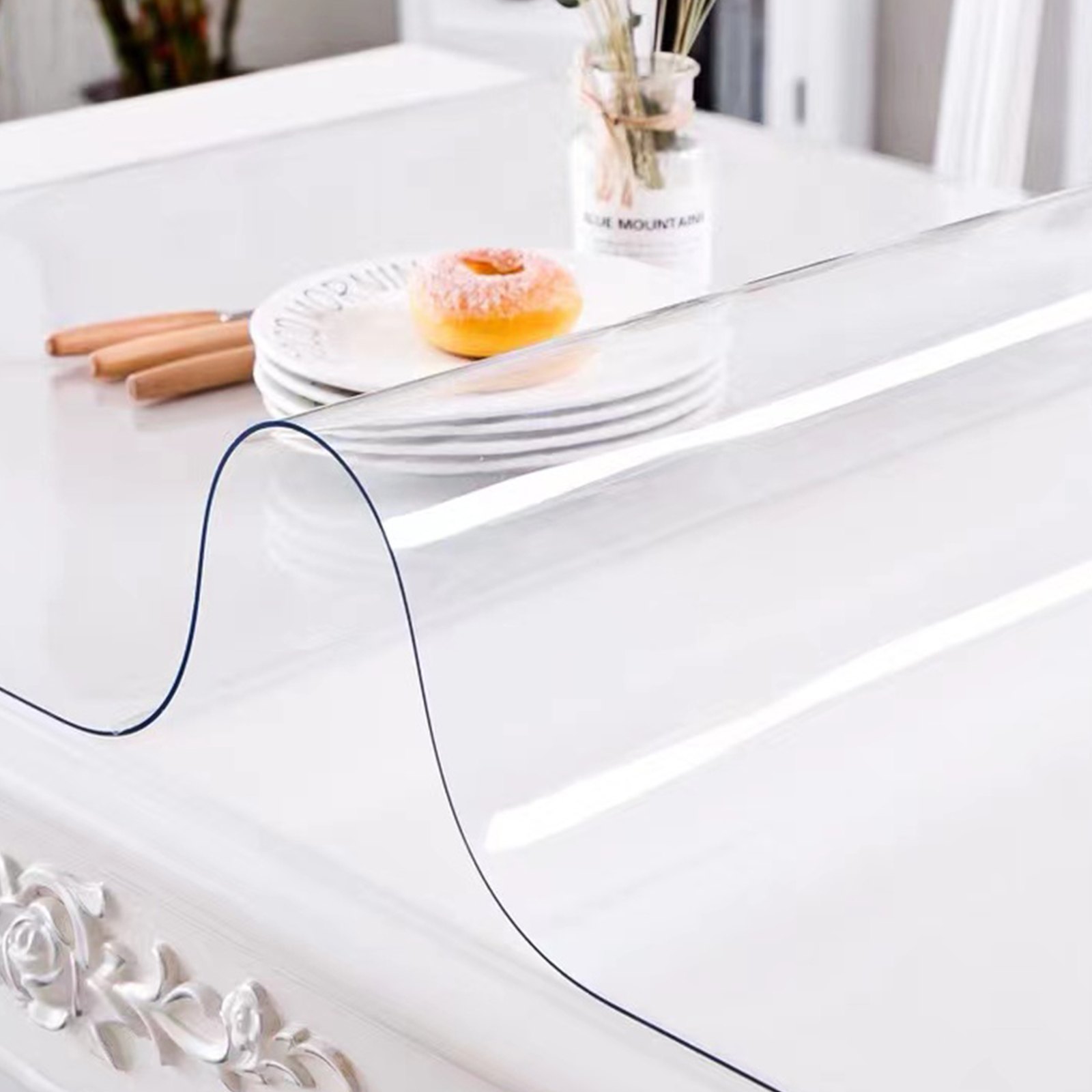 Protector de mesa transparente VEVOR sobre una elegante mesa blanca con platos y una dona en el fondo.