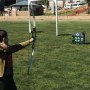 Niño apuntando con un arco a un objetivo de tiro con arco VEVOR en un campo abierto, con varias flechas ya en el objetivo.