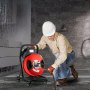 Trabajador que utiliza un desatascador eléctrico VEVOR en un baño alicatado.