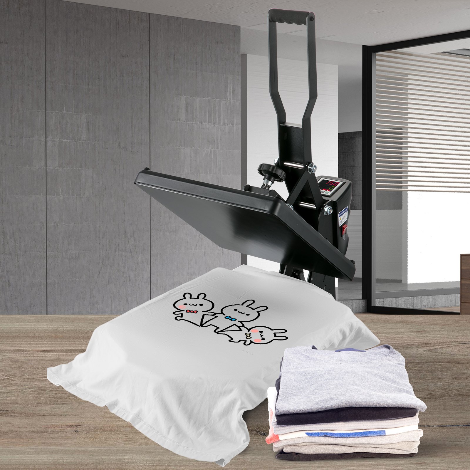 Prensa térmica VEVOR con camiseta impresa y ropa doblada sobre una mesa de madera.