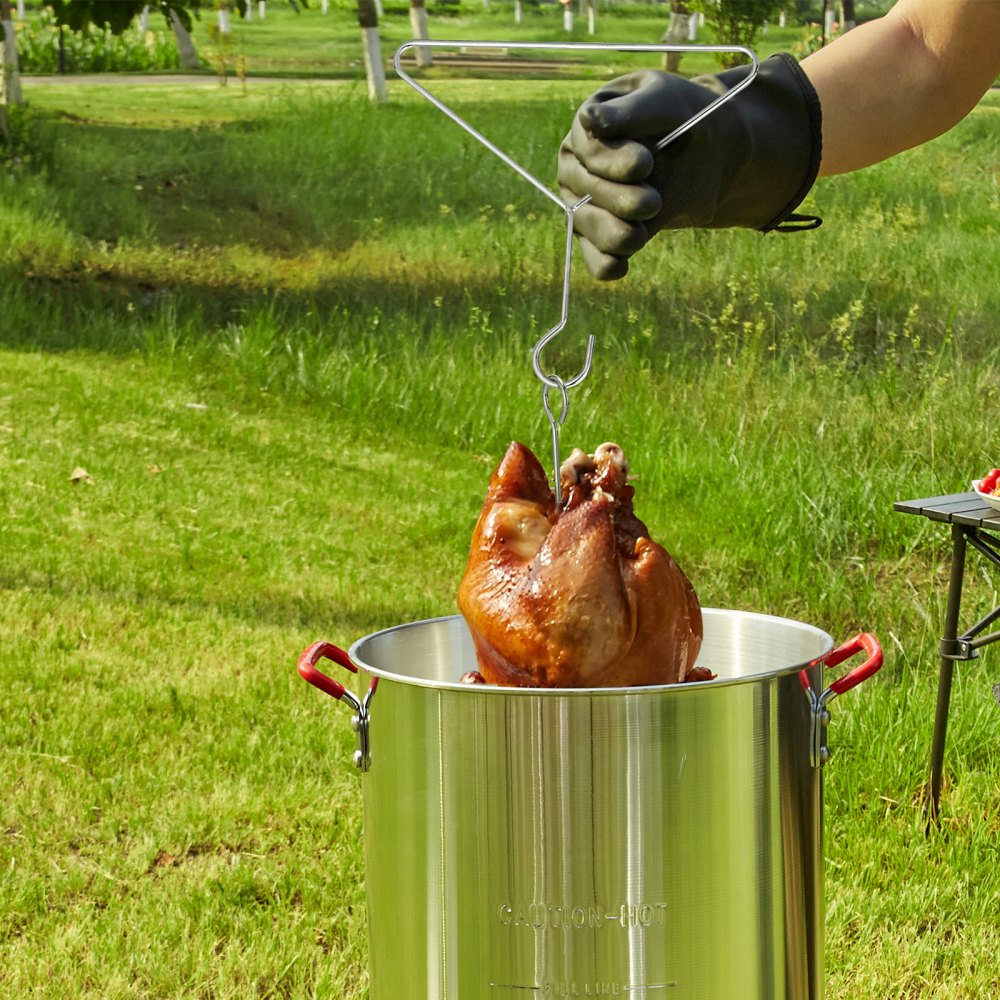 mano enguantada levantando pavo cocido de la freidora de pavo VEVOR de acero inoxidable al aire libre.