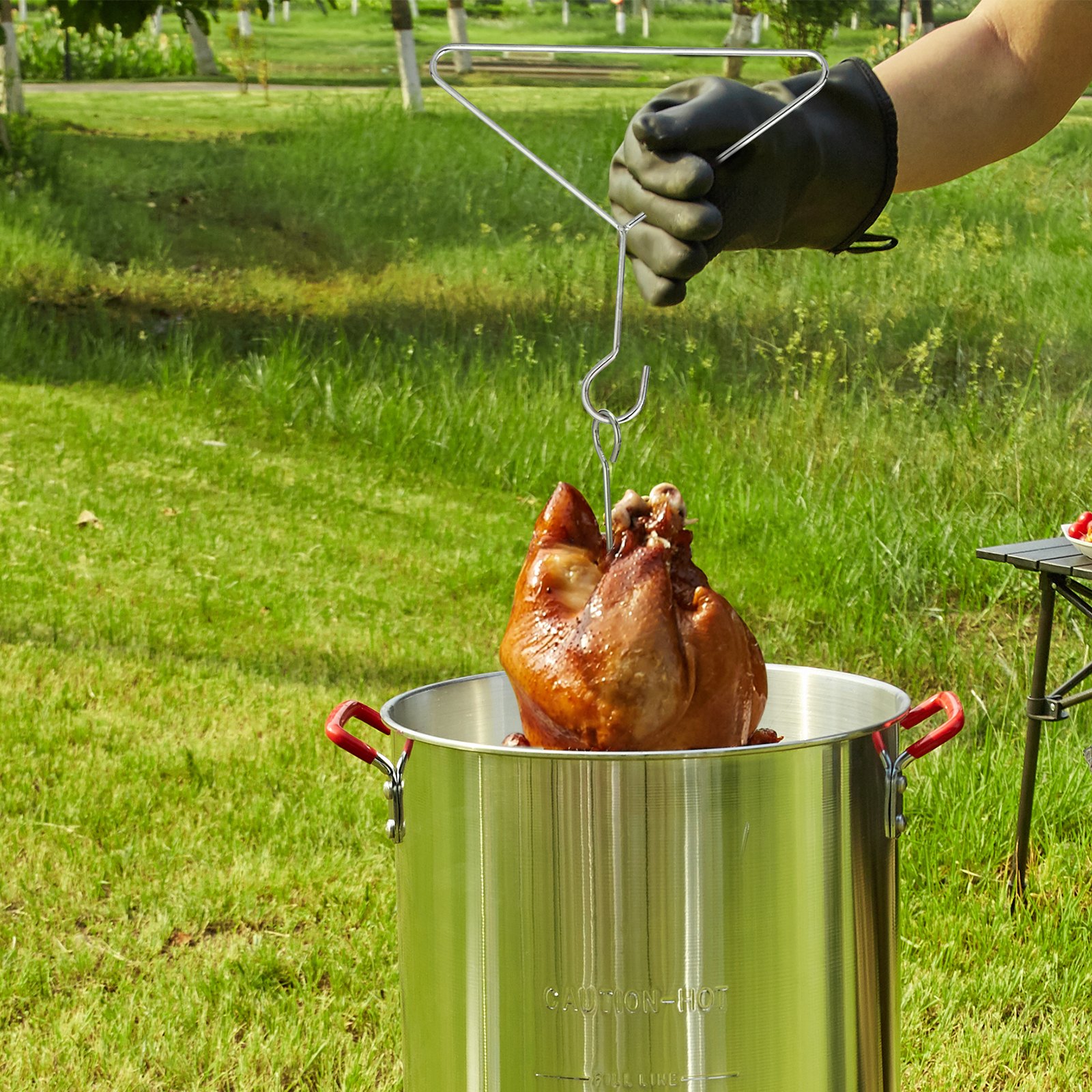mano enguantada levantando pavo cocido de la freidora de pavo VEVOR de acero inoxidable al aire libre.
