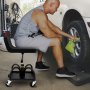 Hombre limpiando un neumático de coche utilizando el taburete de garaje con ruedas VEVOR en un garaje.