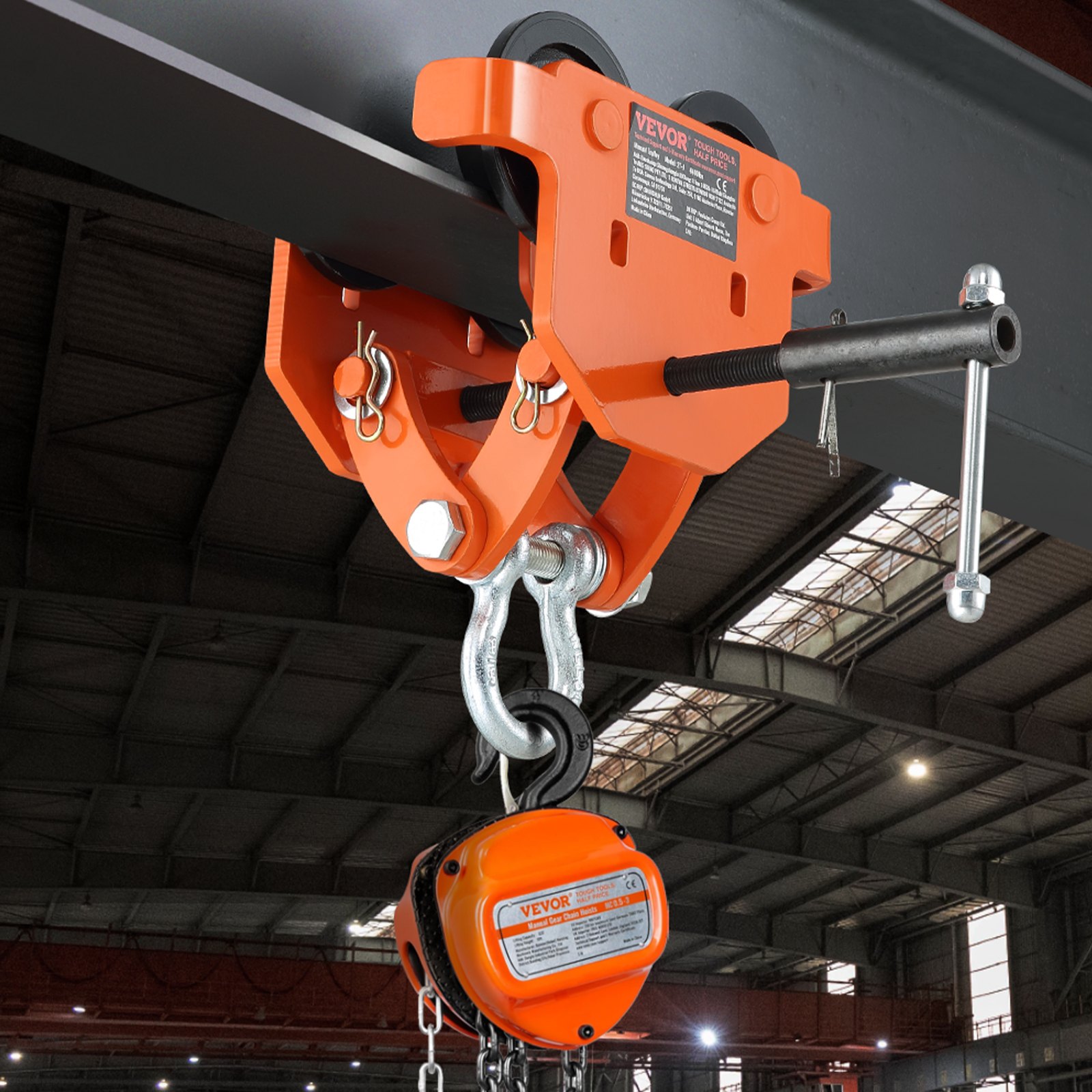 Carro manual VEVOR naranja unido a una viga de acero en el interior de un almacén industrial con luces en el techo.
