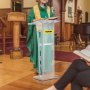 Una persona con una túnica verde se encuentra detrás de un podio de acrílico transparente VEVOR en el interior.