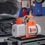 Bomba de vacío HVAC VEVOR en un banco de trabajo en un garaje con el capó de un automóvil abierto al fondo.