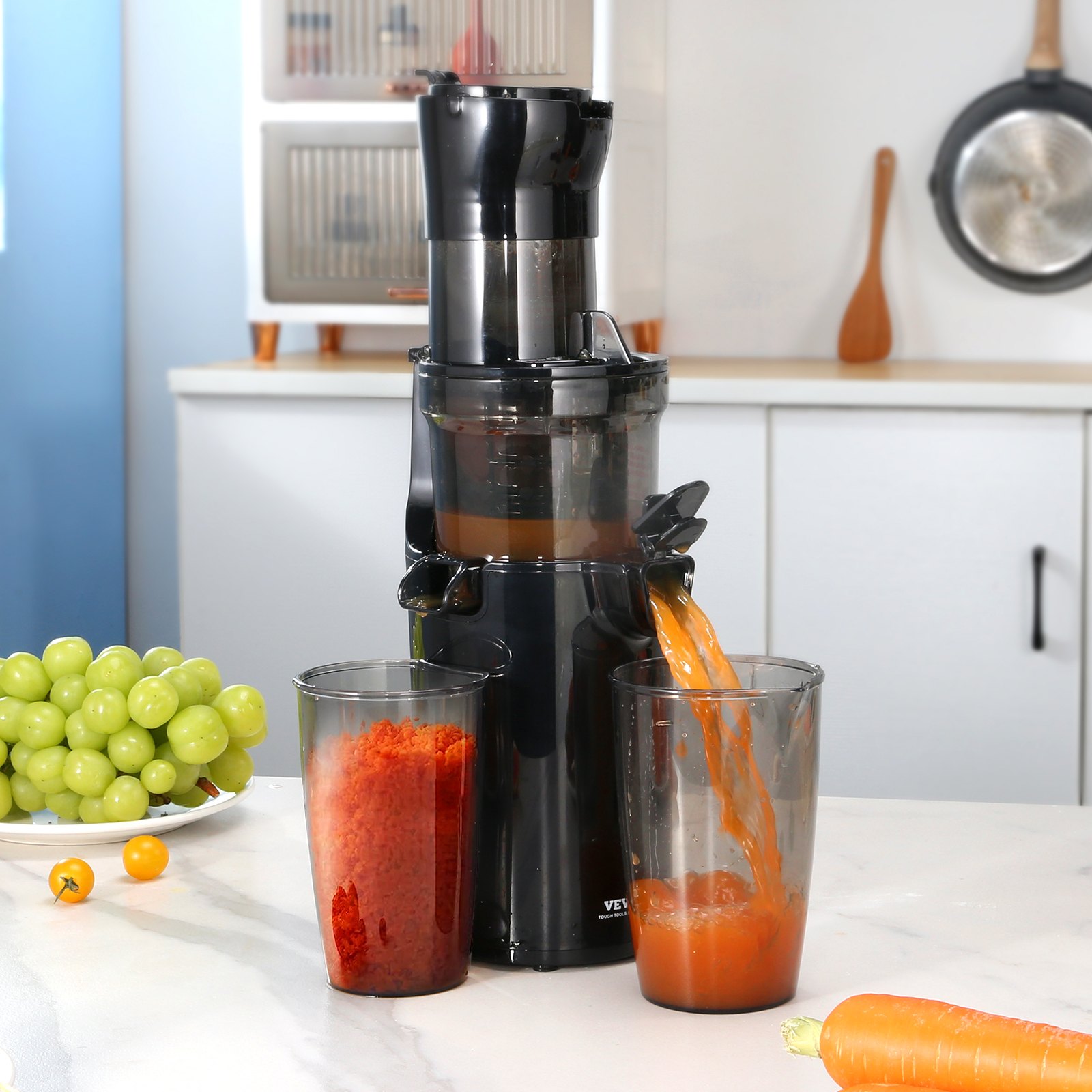 Exprimidor masticador VEVOR sobre la encimera de la cocina exprimiendo zanahorias con uvas y utensilios en el fondo.