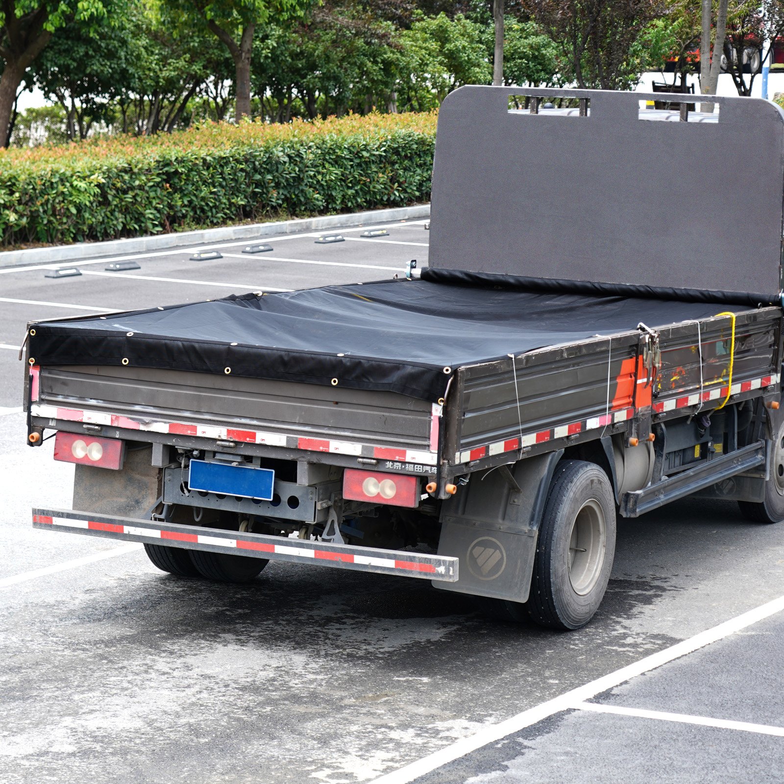 Lona de malla para camión volquete VEVOR que cubre un camión de plataforma, estacionado en un lote al aire libre con árboles en el fondo.