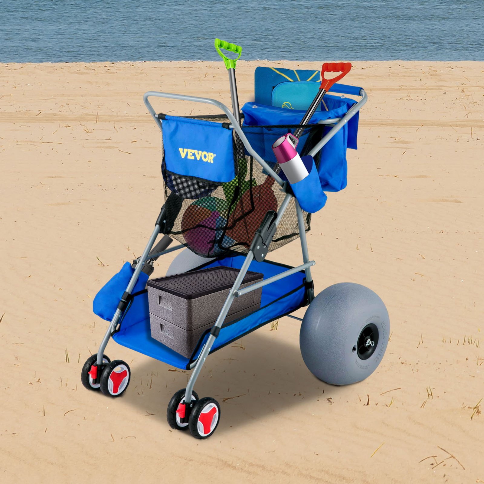 Carrito de playa VEVOR con tela azul, compartimentos de almacenamiento, palas, bolsas de mano y ruedas grandes en una playa de arena.