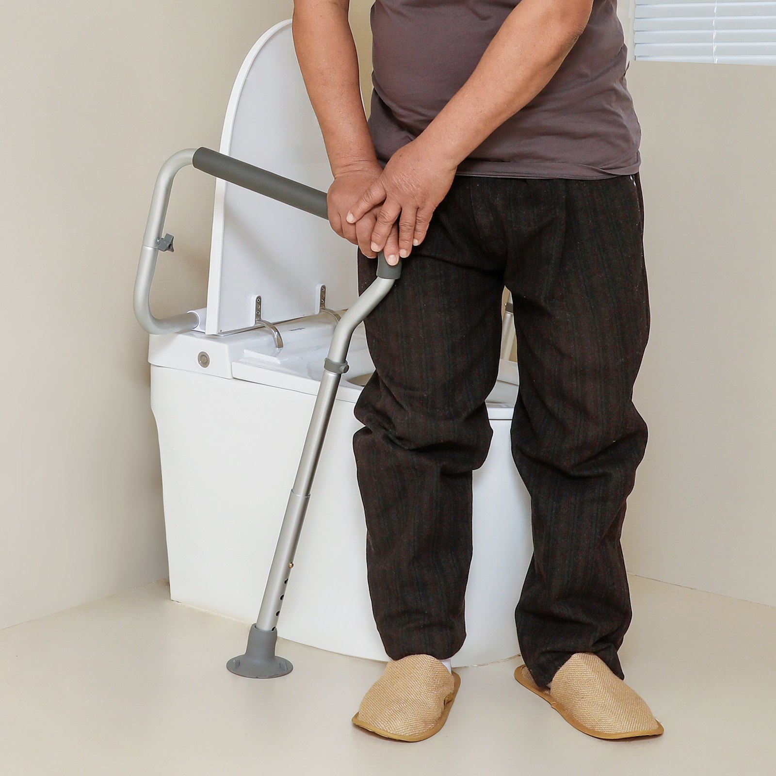 Hombre que usa una barra de seguridad para inodoro VEVOR como apoyo cerca de un inodoro blanco en un baño beige.