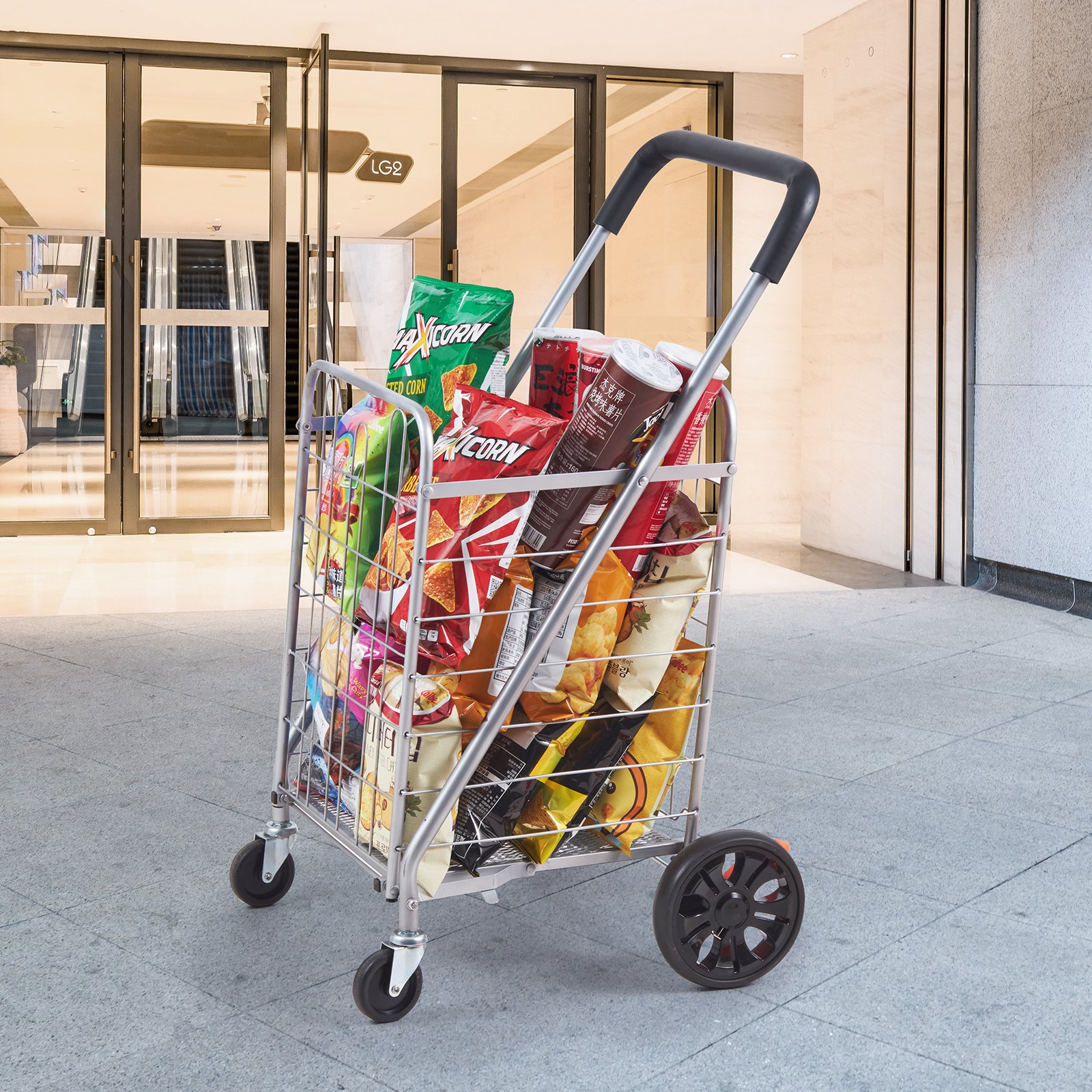 Carrito de compras plegable VEVOR lleno de comestibles afuera de la entrada de un edificio moderno.