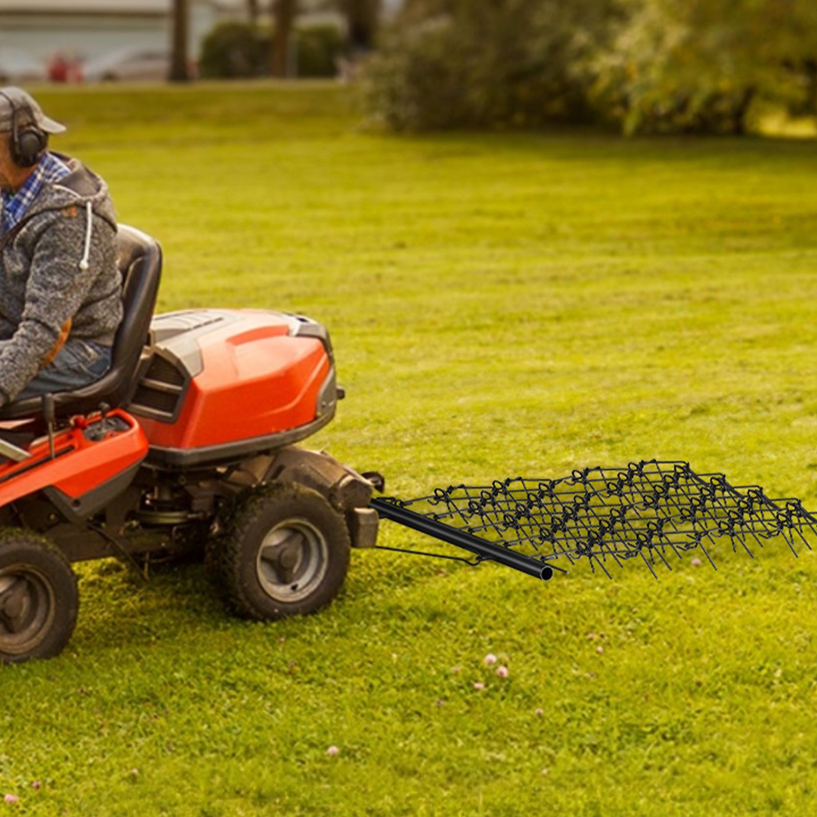 Hombre usando una grada de arrastre VEVOR unida a un tractor cortacésped en un campo verde.