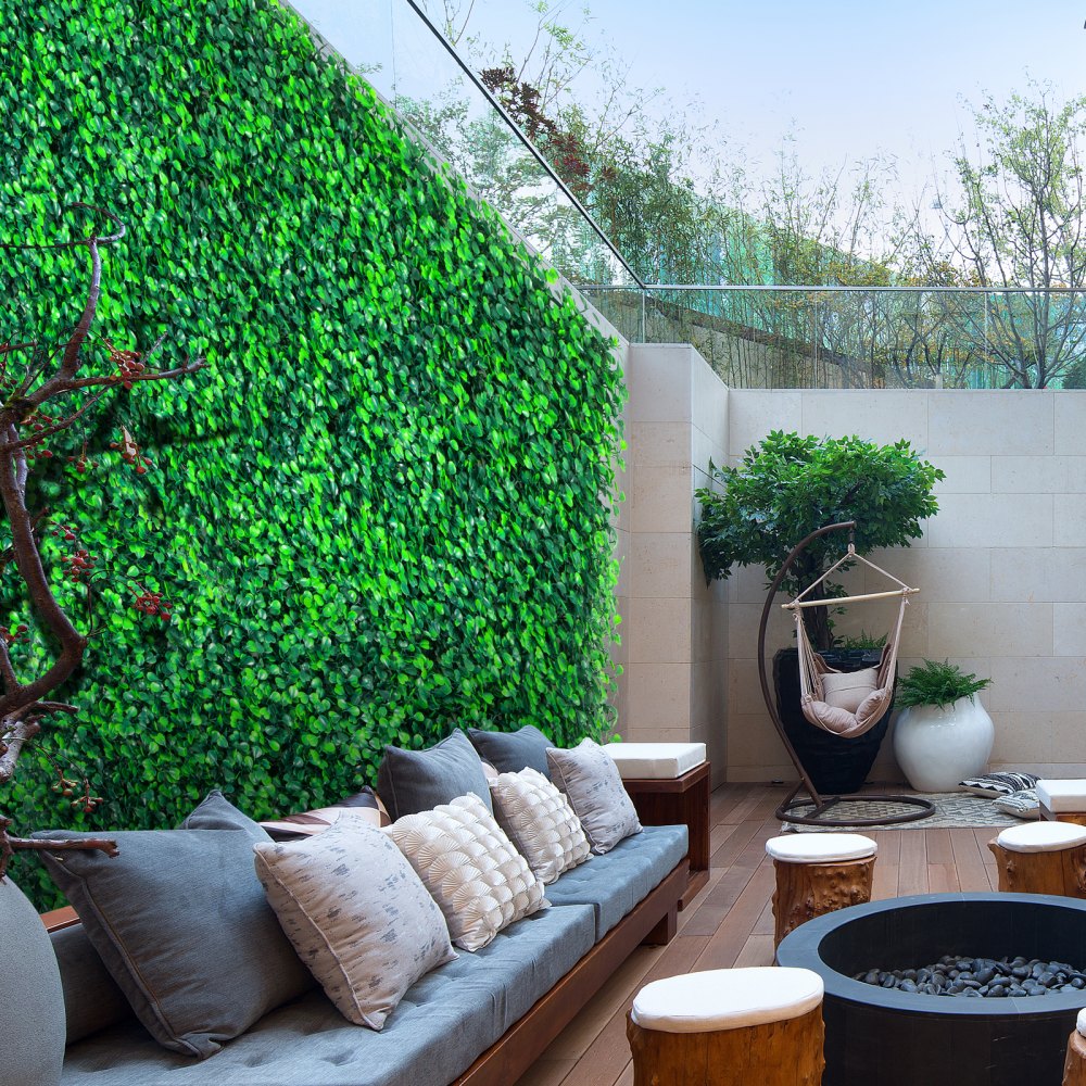 Zona de estar al aire libre con paneles de boj VEVOR, muebles modernos y exuberante vegetación.
